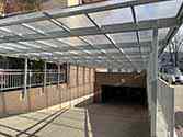 Dak over de oprit naar de ondergrondse parkeergarage van gladde transparante polycarbonaatplaten gemonteerd op draagconstructie van verzinkte staalprofielenn