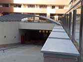 Oprit naar de ondergrondse parkeergarage met dak van polycarbonaat panelen op staalconstructie en glazen balustrade met rvs staanders en leuningen