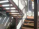 Stalen trap, treden en overloop van houten planken en balustrade met glazen vulling